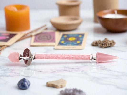 Crystal wand made from rose quarts, on white marble counter top with tarot cards, candles and crystals in the background