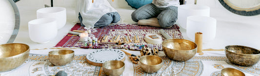 a selection of Tibetan metal singing bowls and white crystal singing bowls on the floor with candles