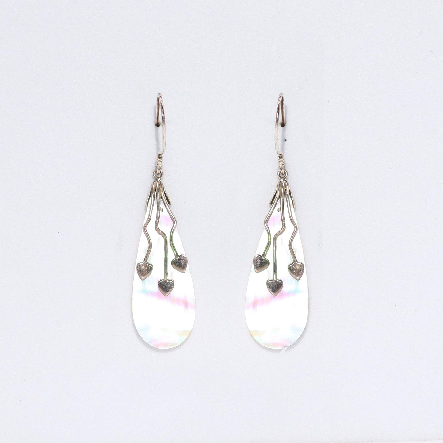 "Long teardrop-shaped mother of pearl earrings with three trailing silver hearts, handcrafted in Bali."