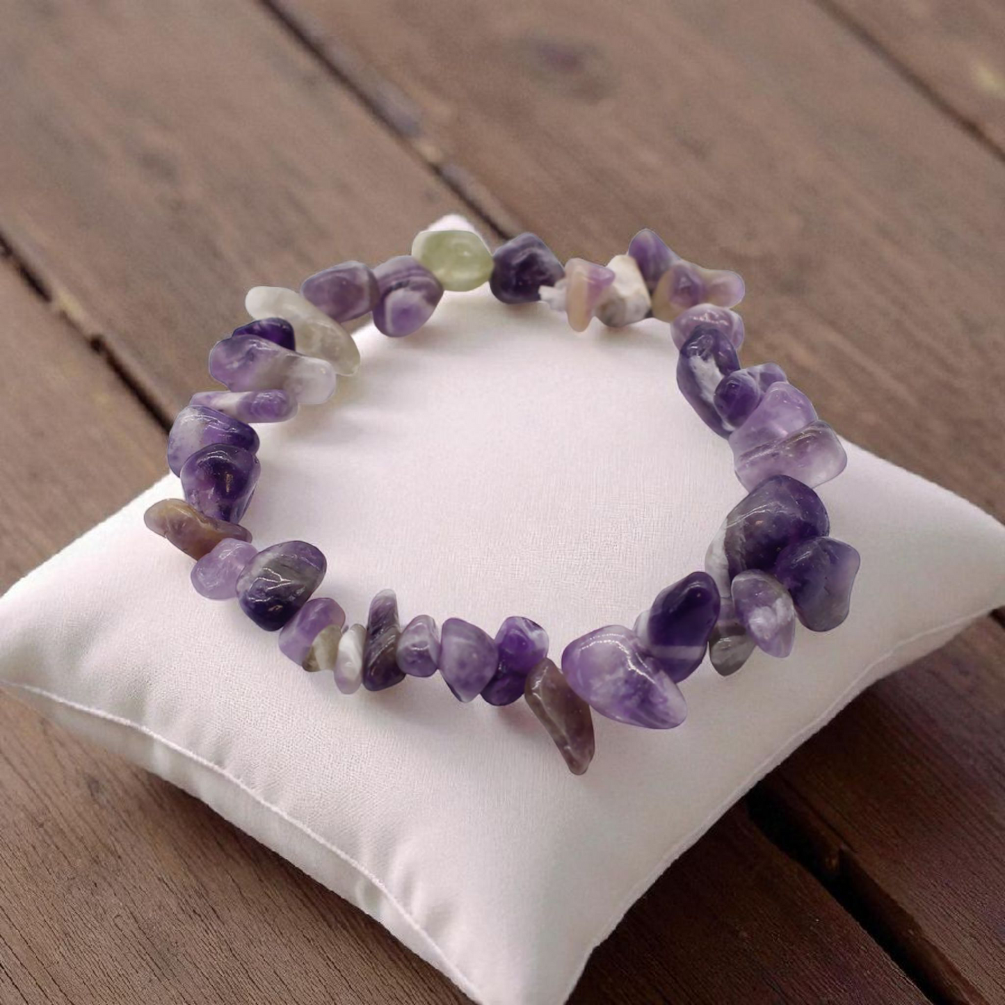 Amethyst chip stone bracelet with soft purple stones, on a pillow on a wood table, symbolising calm, clarity, and spiritual awareness.