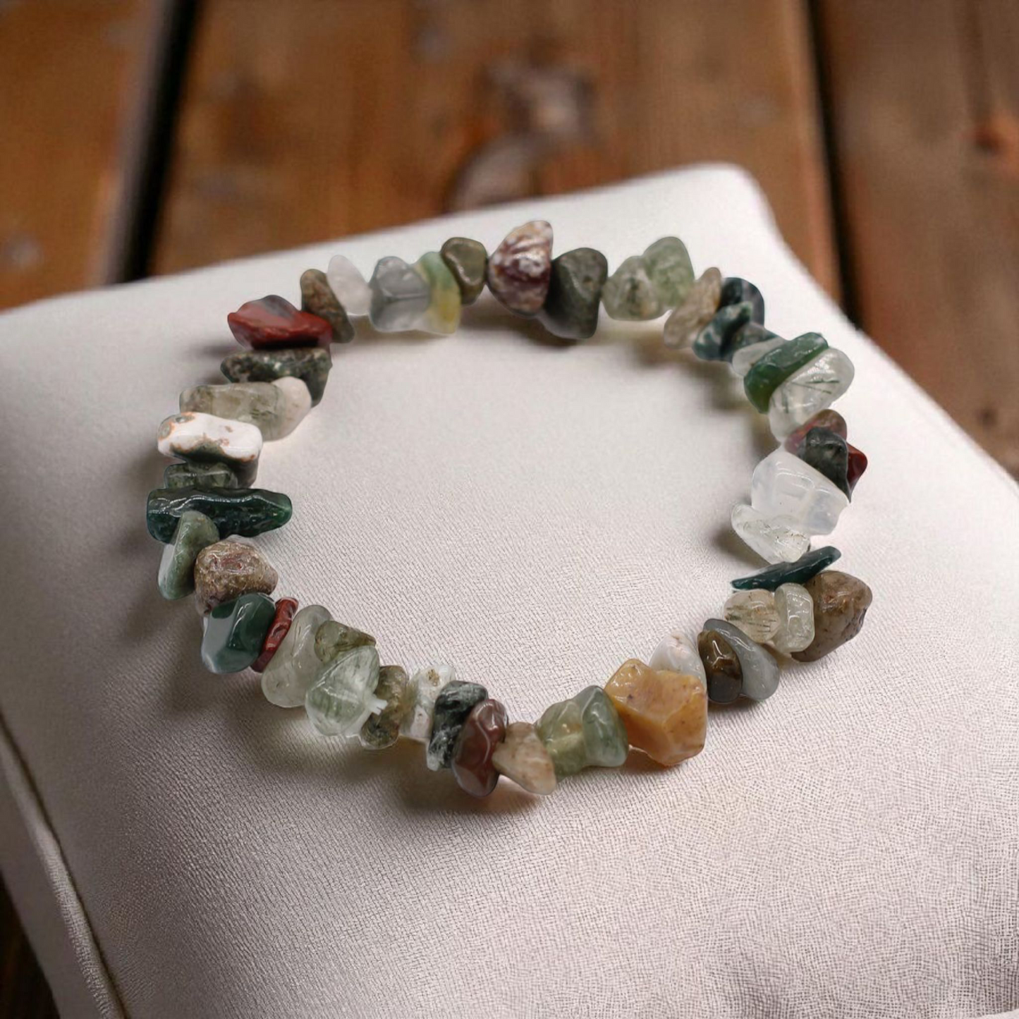 Moss Agate chip stone bracelet with green marbled stones, on a pillow on wood table, symbolising balance, renewal, and connection to nature.