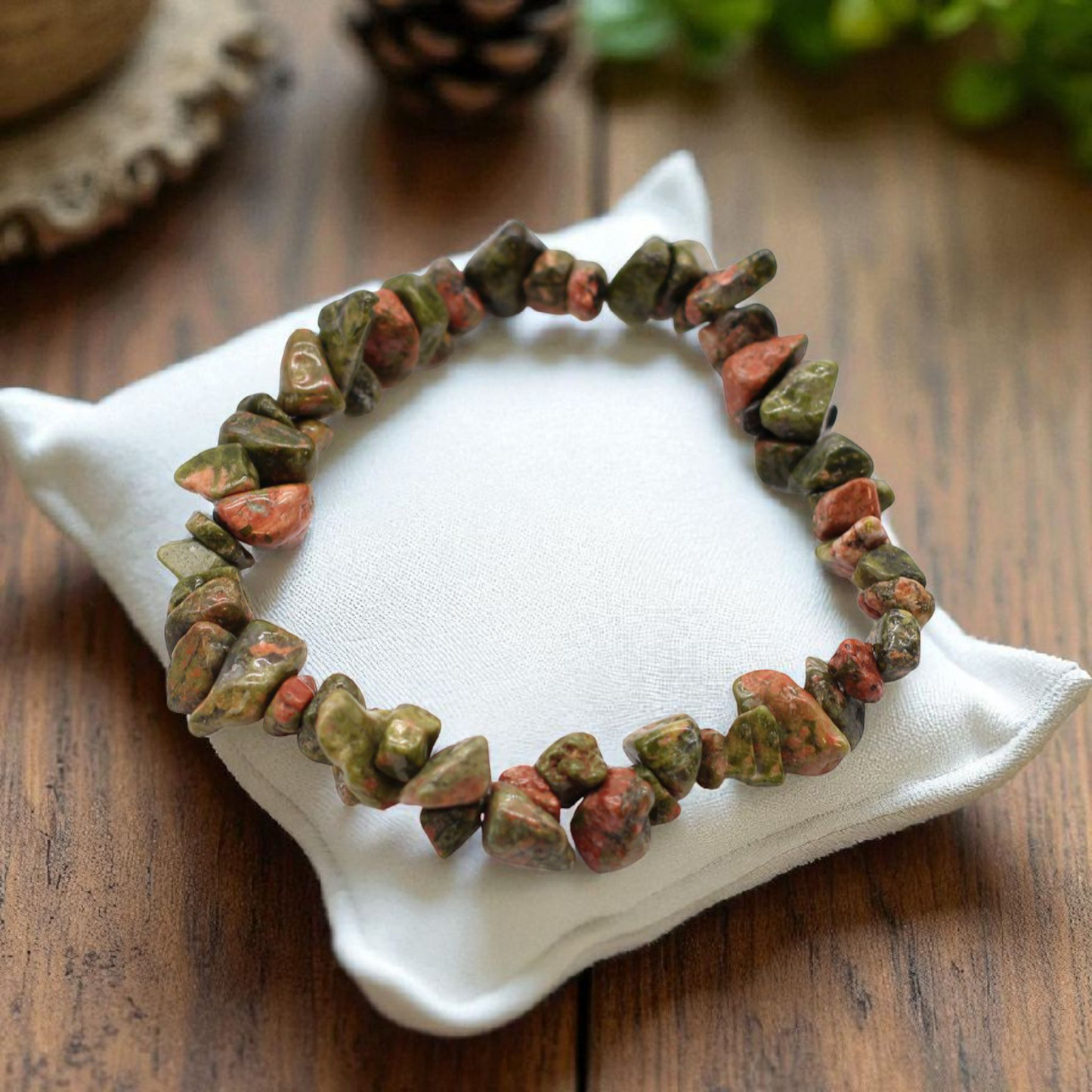 Green Jasper chip stone bracelet with earthy green tones, on a pillow on a wood table, symbolising stability, emotional balance, and gentle renewal.
