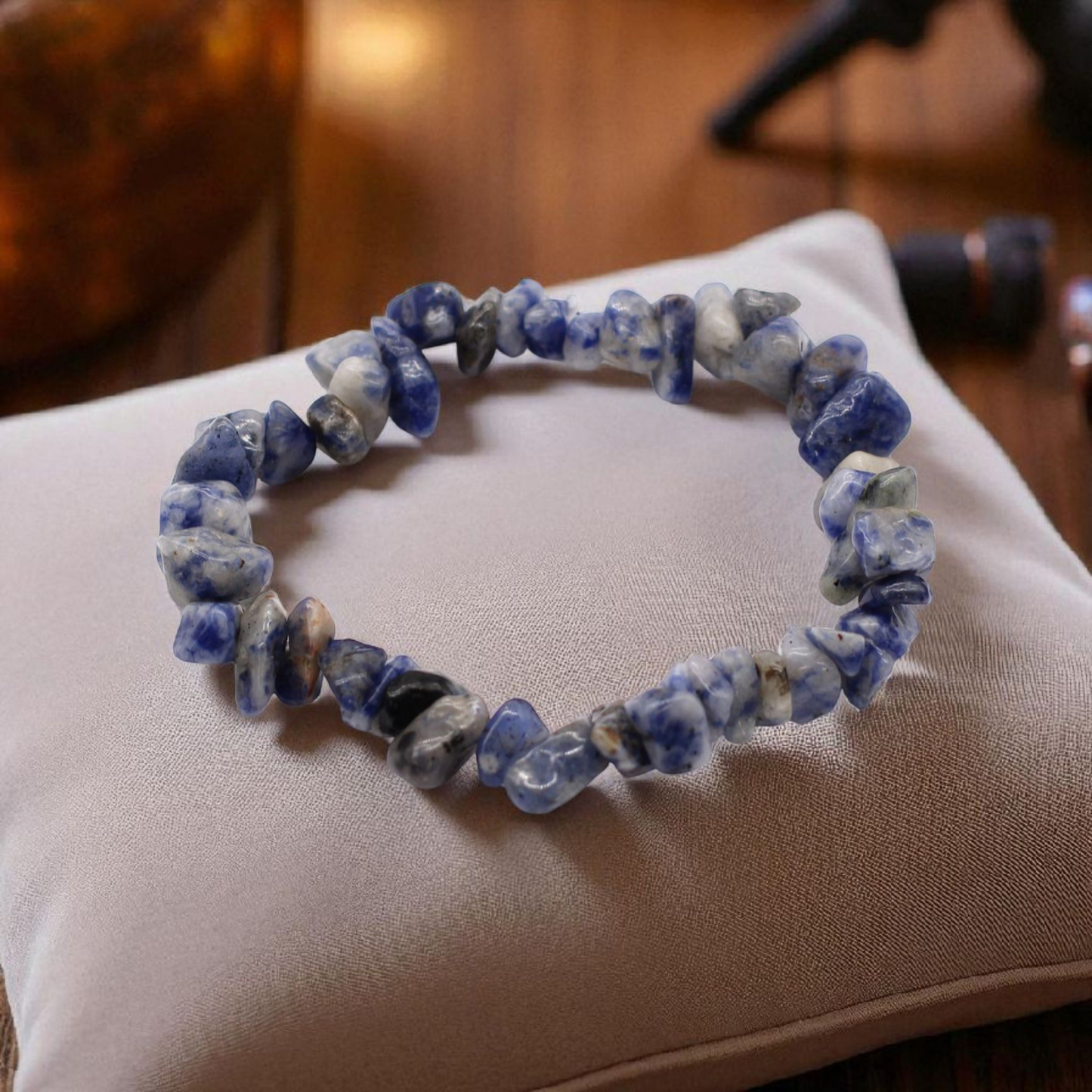Sodalite chip stone bracelet with deep blue and white stones, on a pillow on a wood table, symbolising truth, clarity, and intuitive awareness.