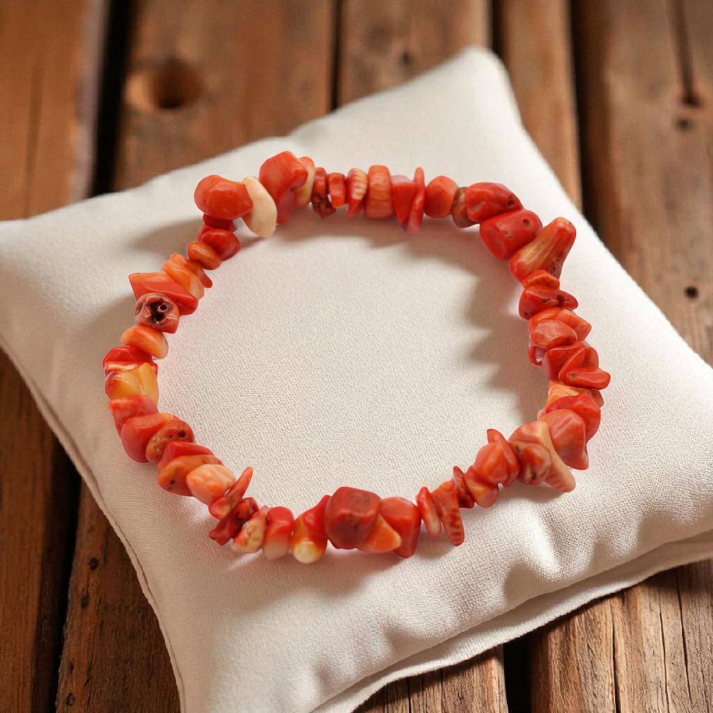 Chip stone bracelet made with redish pink Coralite stones, on pillow on wood table, symbolising vitality, emotional healing, and inner peace.