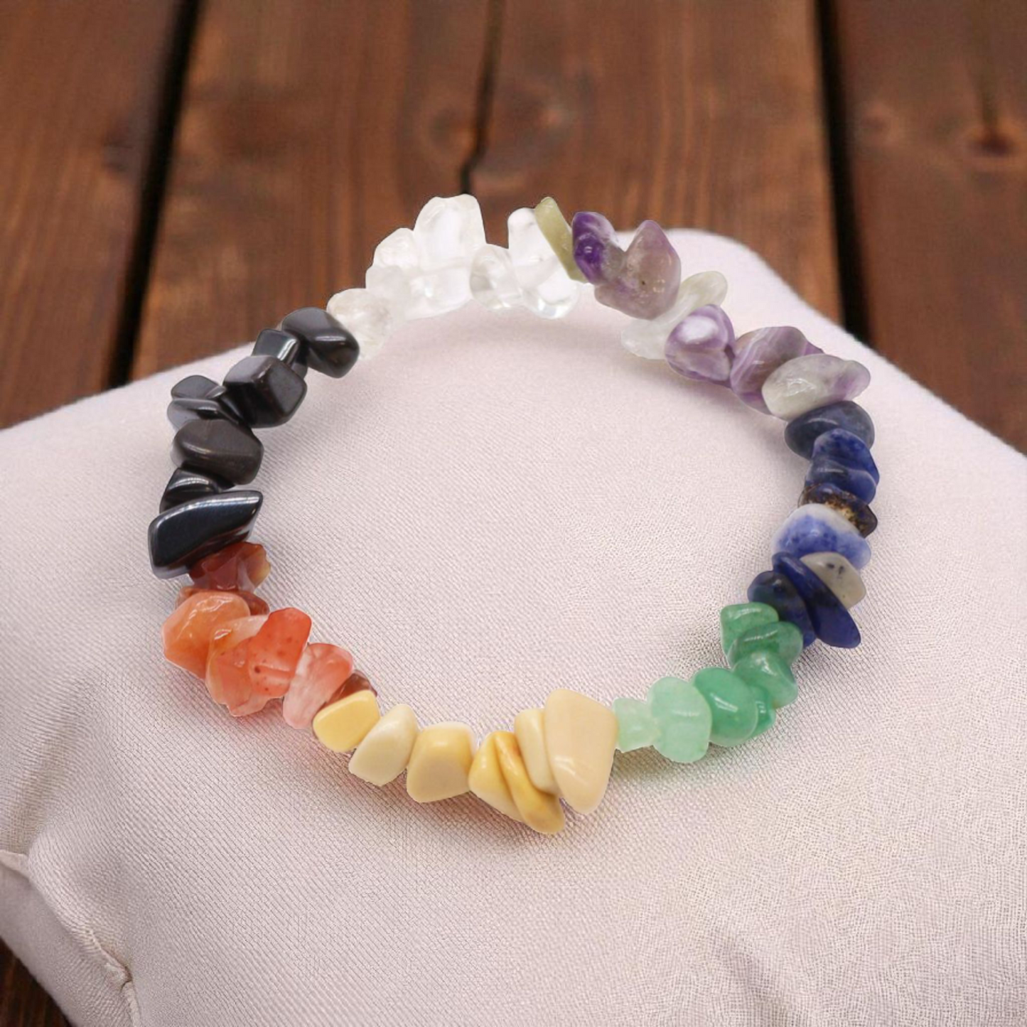 Chip stone chakra bracelet with seven natural gemstones on a pillow on a wood table, designed to align and balance the body’s energy centres.