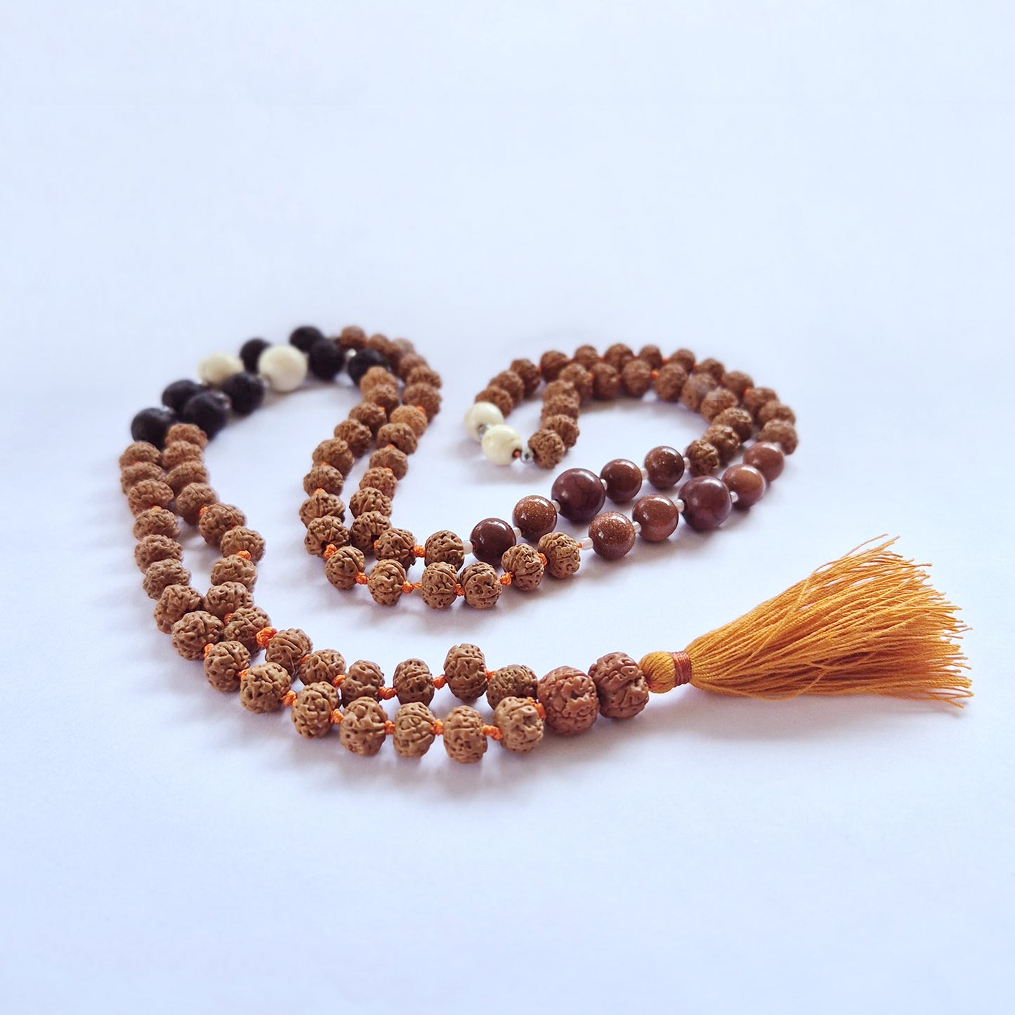 "Earth Element Mala necklace with Rudraksha, volcanic stones, warm red and cream-toned accents, and ochre tassel."