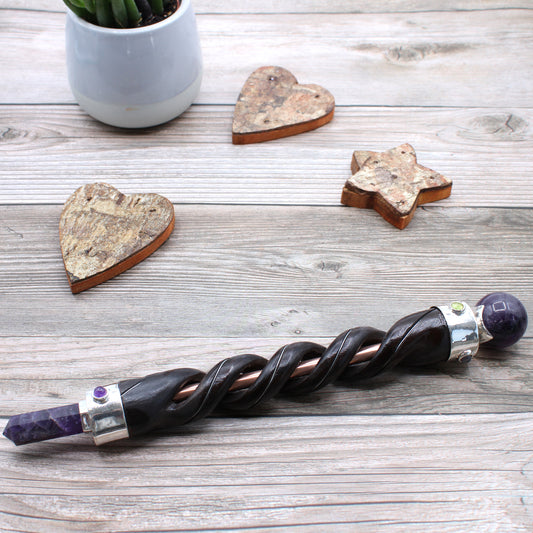 Healing wand with spiral-carved wooden body and central copper pipe, finished with an amethyst point and sphere. Ideal for energy healing and spiritual rituals.