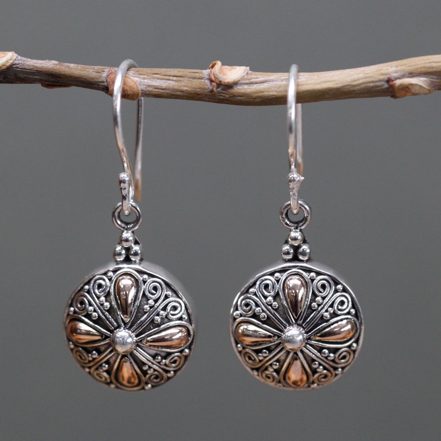 "Round sterling silver earrings with 18k gold teardrop accents and ornate scrollwork, handcrafted in Indonesia."