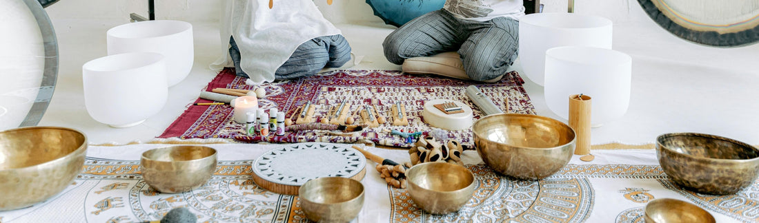 a selection of Tibetan metal singing bowls and white crystal singing bowls on the floor with candles 