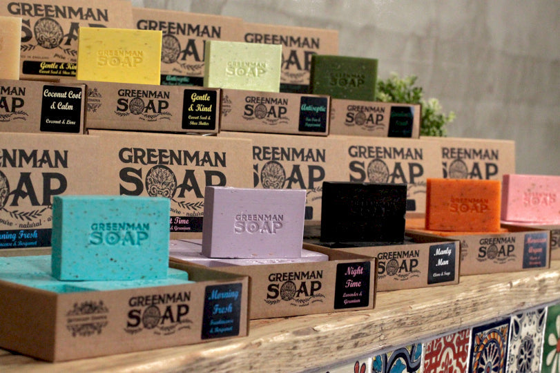 Table display of greenman soap, eight visible different types of soap in various bright colours all with the words "greenman soap" embedded in the front of the soap 
