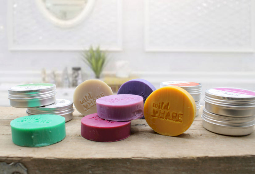 Table display with bars of solid shampoo, various brightly coloured round bars of solid shampoo each one with the words "wild hare" carved into it, come in aluminium tins, 60g