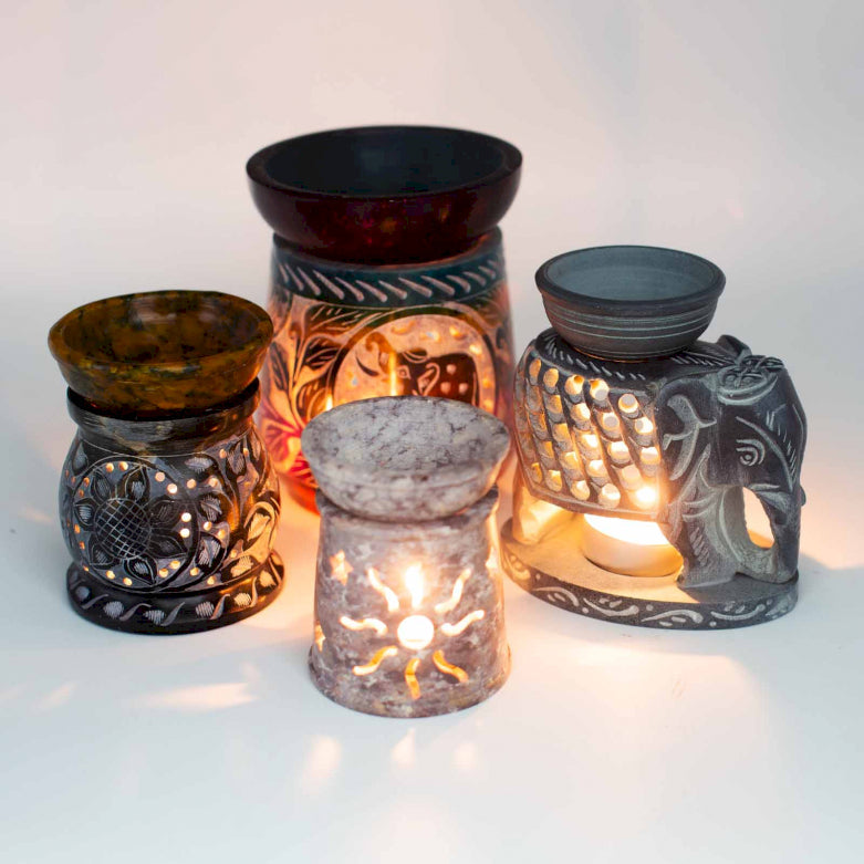 Collection of ceramic and soapstone oil burners, ornate carvings with sun and elephants, tea light candles inside illuminating and casting shadows