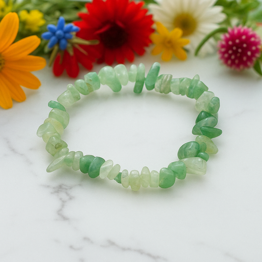 Green Aventurine chip stone bracelet, on a white marble table top with wild flowers in the background, symbolising prosperity, confidence, and emotional growth.

