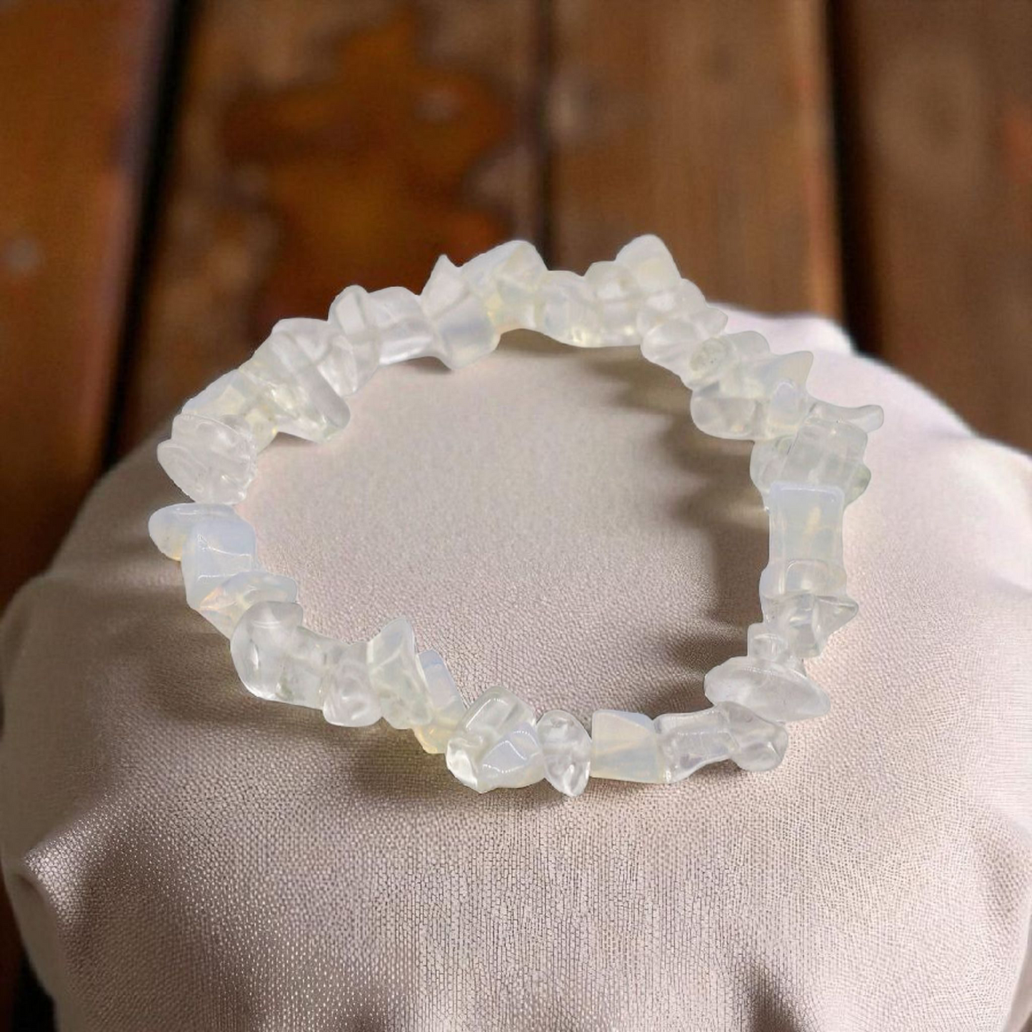 Opalite chip stone bracelet with glowing, translucent beads, on a pillow on wood table, symbolising clarity, emotional balance, and calm transformation.
