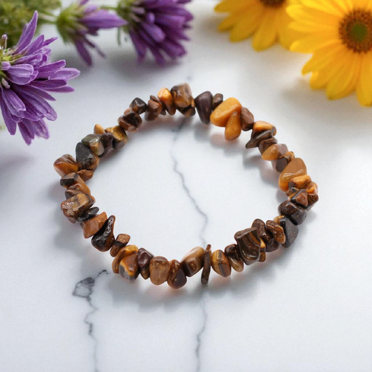 Tiger’s Eye chip stone bracelet with golden-brown stones, on a white marble table top with wild flowers in the background, symbolising confidence, protection, and grounded strength.

