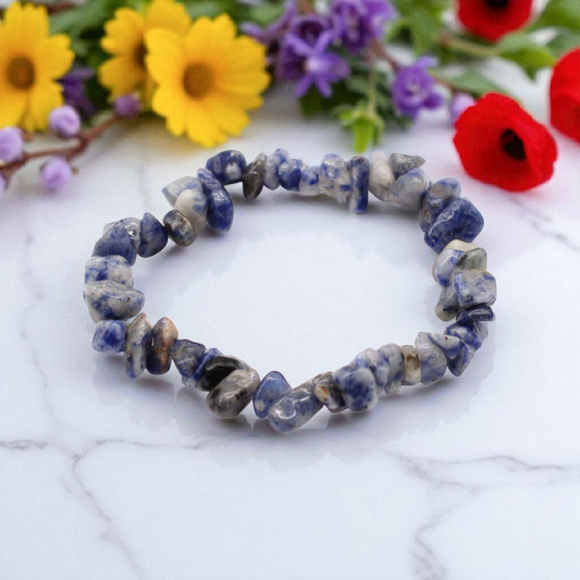 Sodalite chip stone bracelet with deep blue and white stones, on a white marble table top with wild flowers in the background, symbolising truth, clarity, and intuitive awareness.
