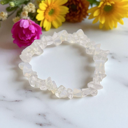 Opalite chip stone bracelet with glowing, translucent beads, on a white marble table top with wild flowers in the background, symbolising clarity, emotional balance, and calm transformation.
