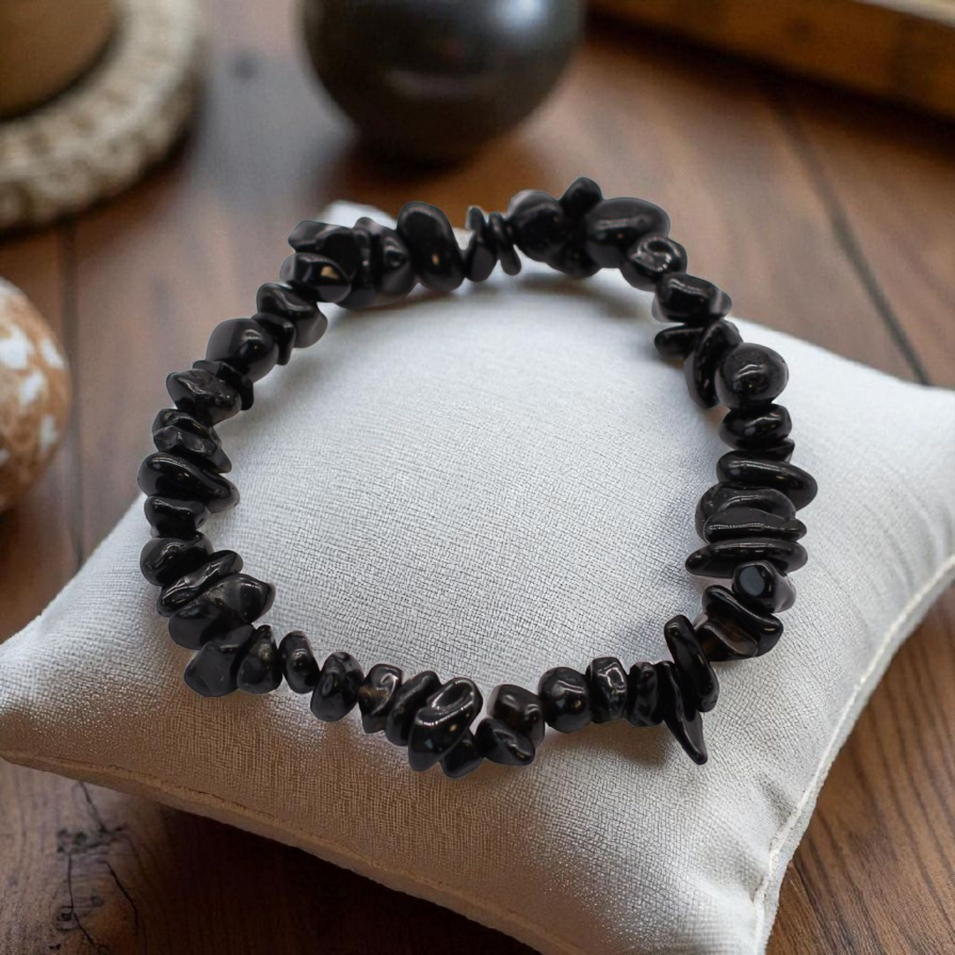 Black Agate chip stone bracelet with deep black stones, on a pillow on a wood table, symbolising protection, grounding, and emotional resilience.
