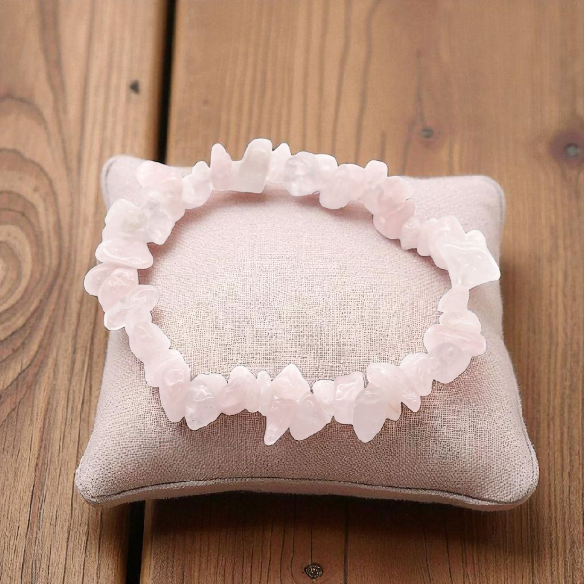 Rose Quartz chip stone bracelet with soft pink stones, on a pillow on a wood table, symbolising love, compassion, and emotional healing.
