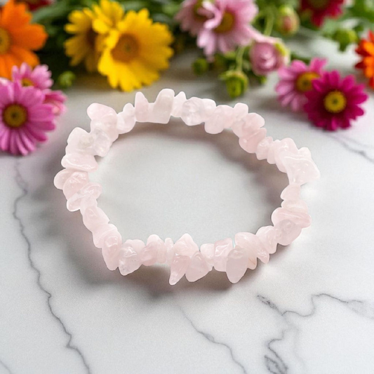 Rose Quartz chip stone bracelet with soft pink stones, on a white marble table top with wild flowers in the background, symbolising love, compassion, and emotional healing.
