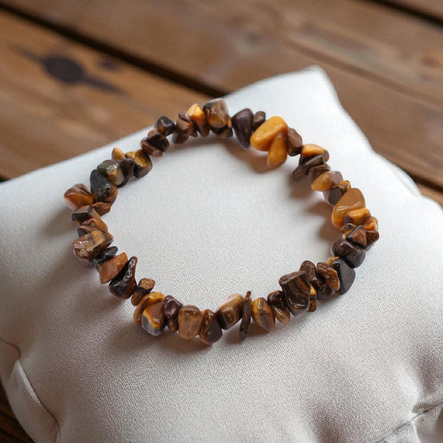 Tiger’s Eye chip stone bracelet with golden-brown stones, on a pillow on a wood table, symbolising confidence, protection, and grounded strength.
