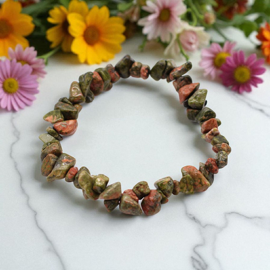 Green Jasper chip stone bracelet with earthy green tones, on a white marble table top with wild flowers in the background, symbolising stability, emotional balance, and gentle renewal.
