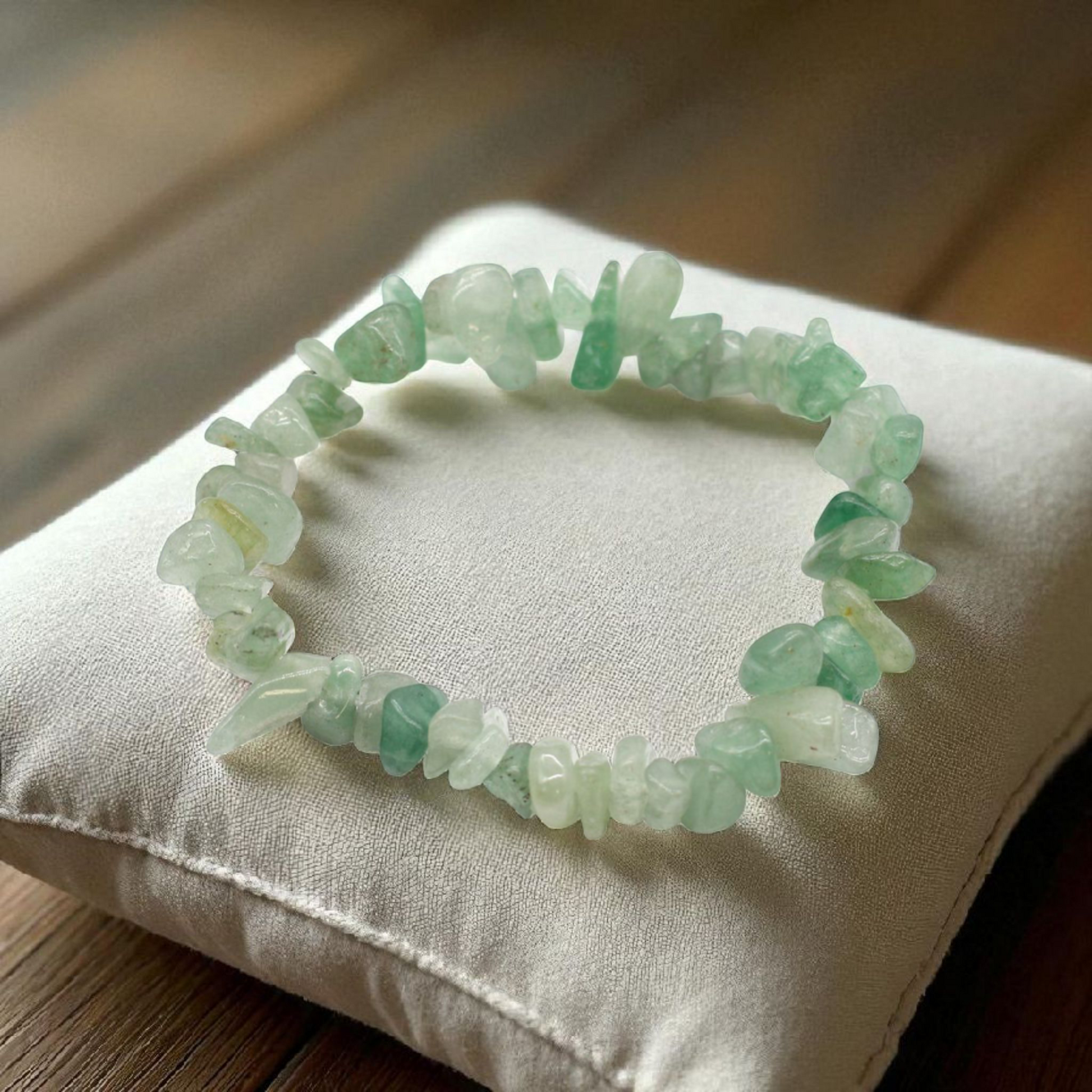 Green Aventurine chip stone bracelet, on a pillow on a wood table, symbolising prosperity, confidence, and emotional growth.
