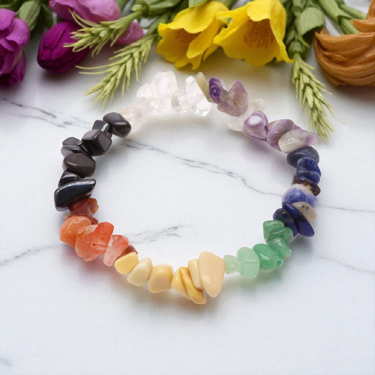 Chip stone chakra bracelet with seven natural gemstones, onwhite marble table top with wild flowers in the background, designed to align and balance the body’s energy centres.
